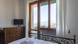 A bedroom with a bed, a wooden dresser, a television on the dresser, and a window with a view of the city and mountains. - JOIVY Front Sea Apt With Big Terrace In Chiavari (Chiavari)