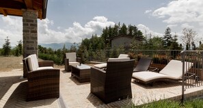 An outdoor patio with wicker furniture, a stone pillar, and a view of a mountain and trees. - JOIVY Superb Villa For 7 W/Backyard And Bbq Area In Vaccarezza (Bobbio)