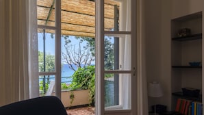 An open door leading to a balcony with a view of the sea, a chair, a table, and a bookshelf. - JOIVY Villa W/Superb View And Private Garden In Mulinetti (Recco)