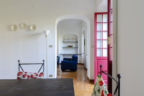 Une pièce comprenant une table à manger, une chaise bleue, une porte rouge et un couloir menant à une autre pièce où se trouve un canapé bleu.