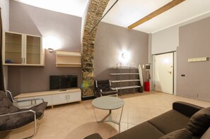 A modern living room with a sofa, a TV, a stone pillar, and a staircase. - JOIVY Warm Family Flat For 9, Near Porto Antico (Genoa)