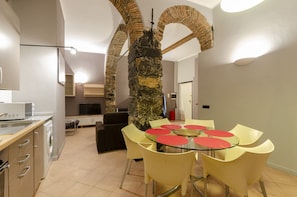 A modern kitchen with a dining area, featuring a stone pillar, a washing machine, and a flat-screen TV. - JOIVY Warm Family Flat For 9, Near Porto Antico (Genoa)