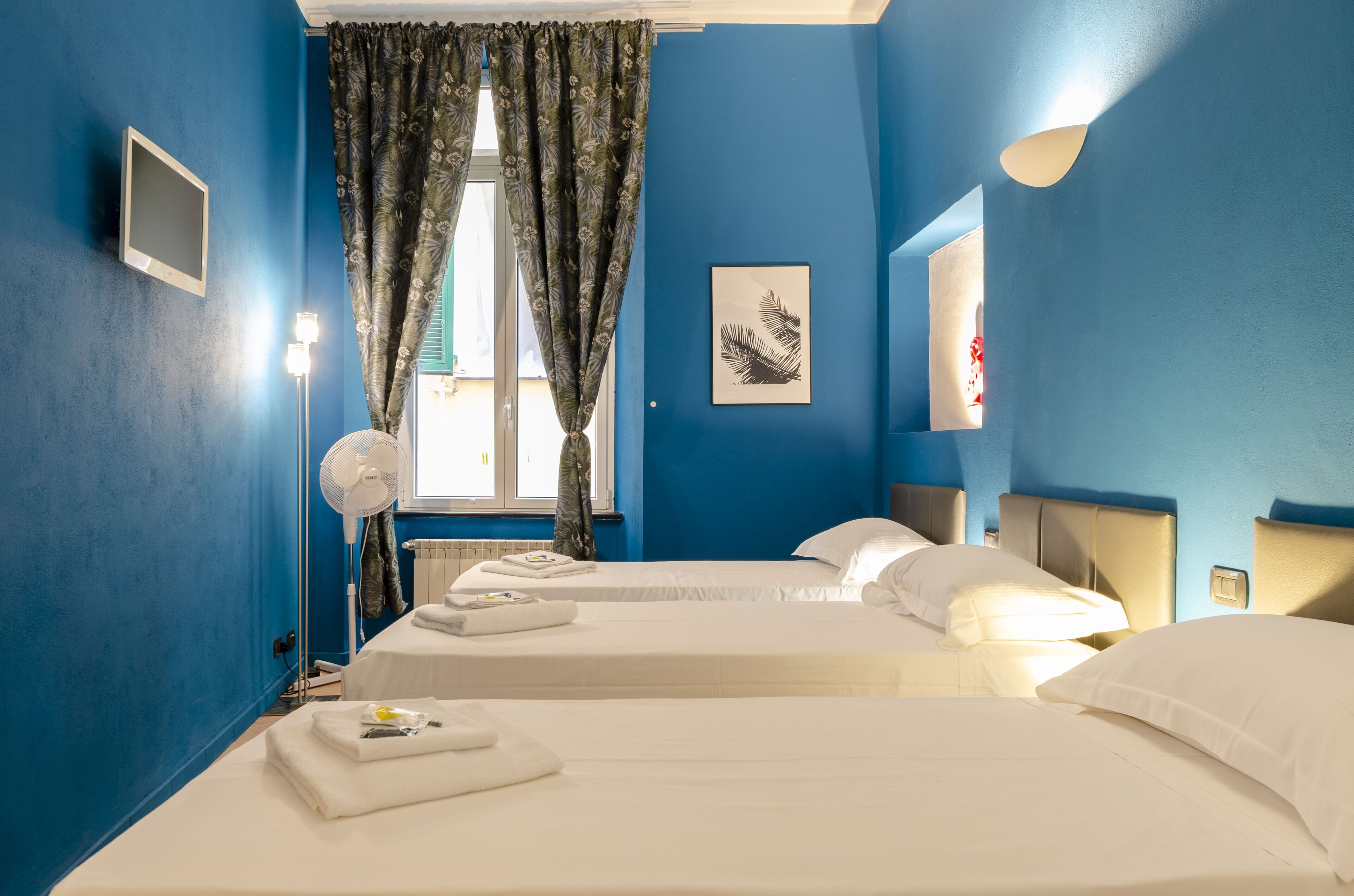 Ett hotellrum med två sängar, ett fönster med gardiner, en tavla på väggen och en sänglampa.