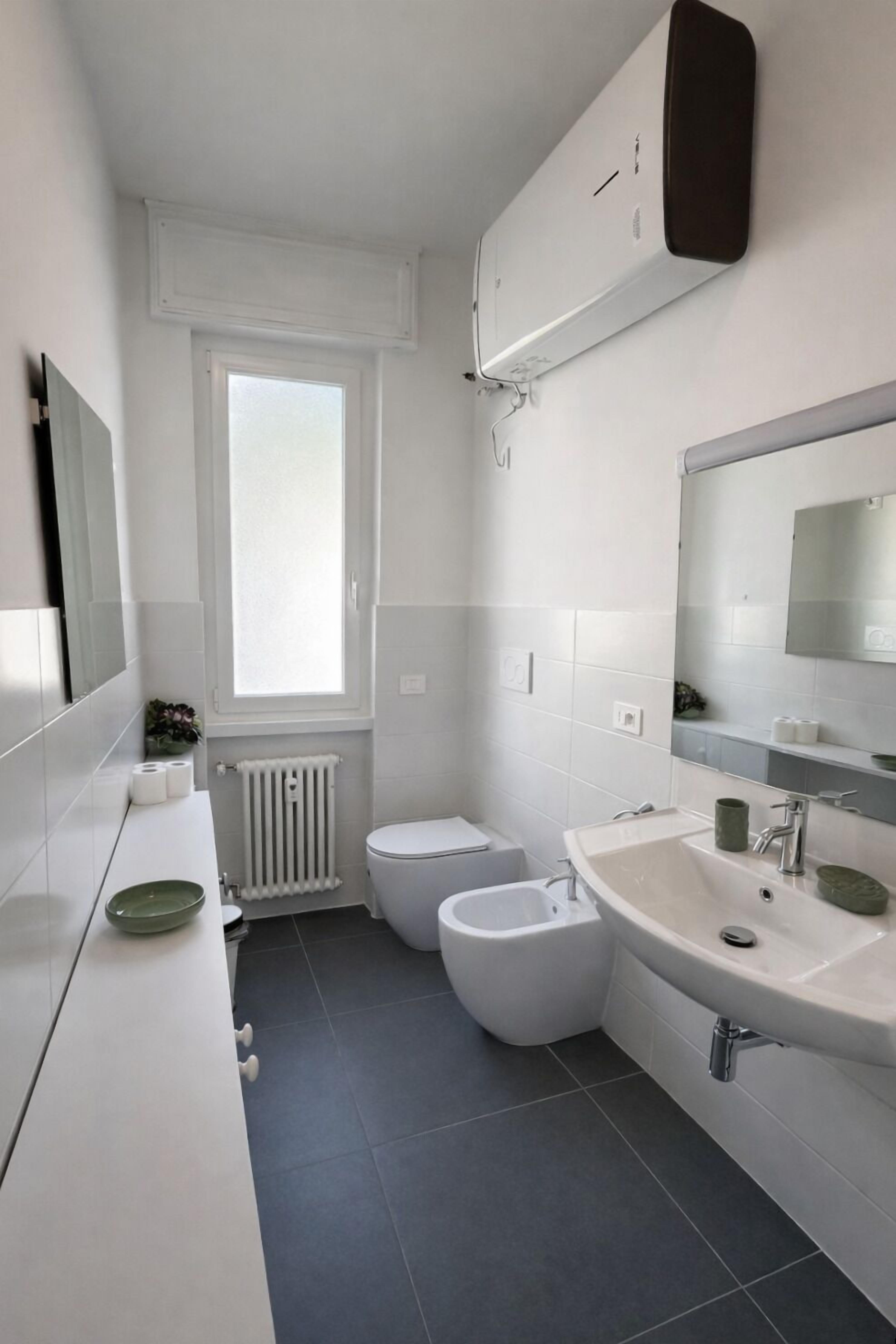 A modern bathroom with a toilet, bidet, sink, and a large mirror.