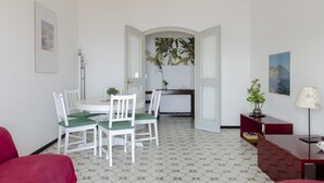 Un coin repas avec une table et des chaises blanches, une petite plante et un tableau accroché au mur.