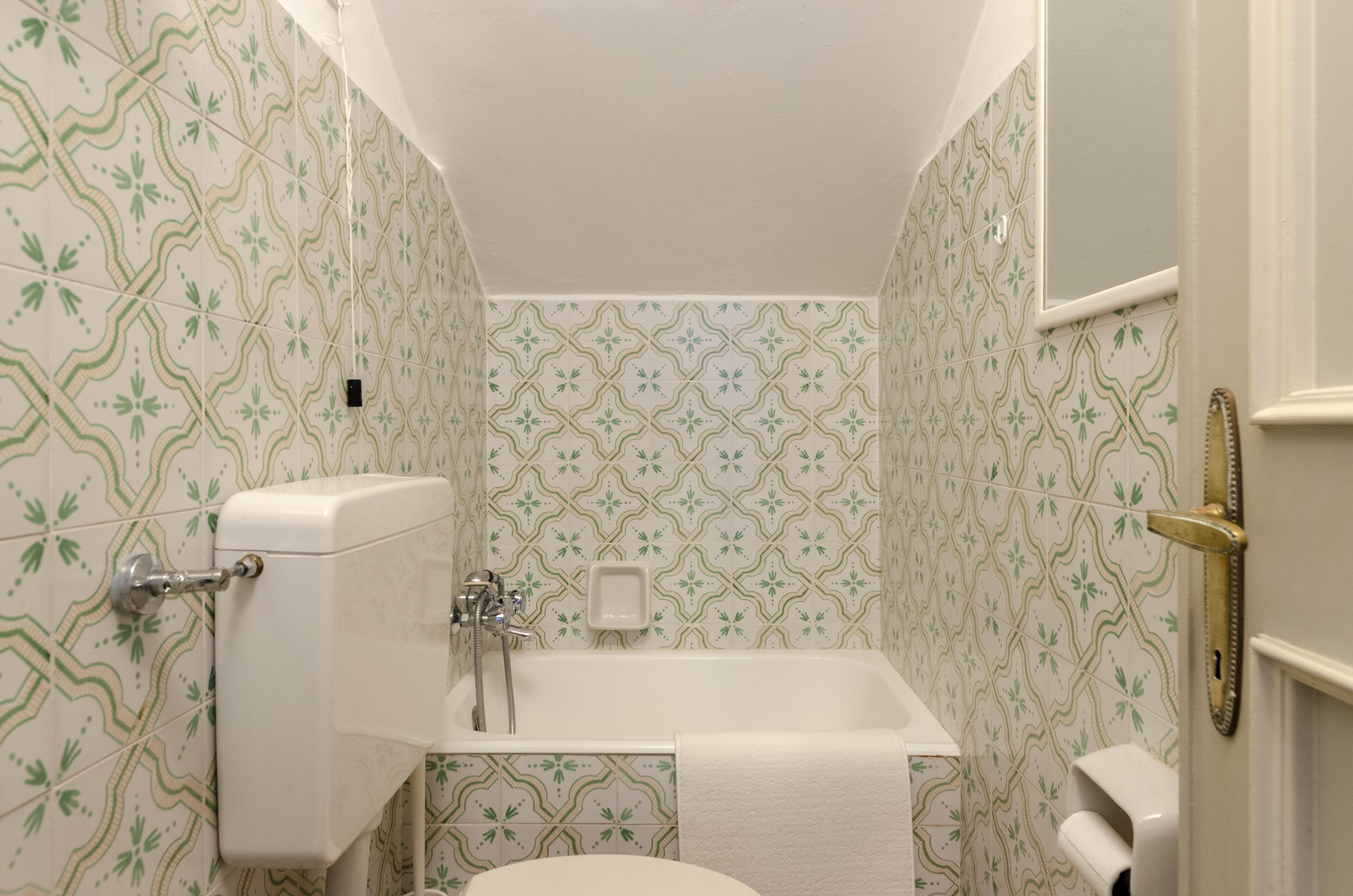 A bathroom with a toilet, sink, and bathtub. The walls have a green and white patterned tile design.