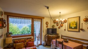 Ein gemütliches Wohnzimmer mit einer Couch, einem Esstisch mit Stühlen, einem Fernseher und einem Fenster mit Vorhängen.