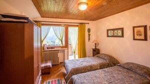 Ein Schlafzimmer mit zwei Betten, Holzboden, Heizkörper, Schreibtisch und einem Fenster mit Vorhängen.