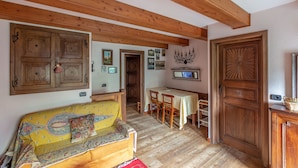 Un salon chaleureux avec un plafond en bois, un canapé recouvert d’un tissu à motifs, une table à manger avec des chaises et une porte en bois.