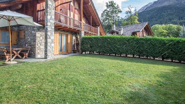 Un chalet en bois avec des fondations en pierre, un balcon et une pelouse bien entretenue.