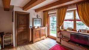 Une pièce chaleureuse avec des poutres apparentes, une grande fenêtre avec des rideaux, un meuble en bois, un téléviseur et un radiateur.