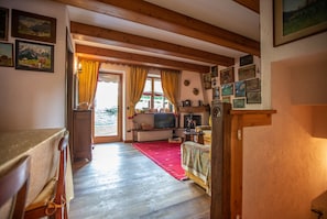 Una habitación acogedora con vigas de madera, chimenea, televisor y alfombra roja.