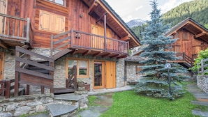 Un chalet en bois, doté de fondations en pierre, de balcons en bois et d’un escalier en pierre menant à l’entrée.