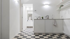 Een moderne keuken met een zwart-wit geruite vloer, witte kasten, een roestvrijstalen spoelbak en een ophangende handdoek.