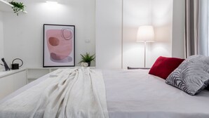 Een moderne hotelkamer met een net opgemaakt bed, een bedlampje, een lijst met abstracte kunst en een kleine potplant.