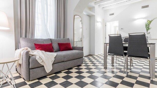 Een moderne woonkamer met een grijze bank, rode kussens, een kleine ronde tafel en een zwart-wit geruit vloerkleed.