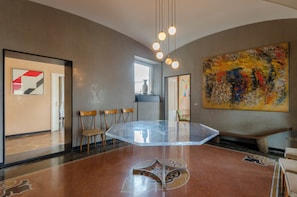 A modern interior with a glass-top table, wooden chairs, and a large abstract painting.