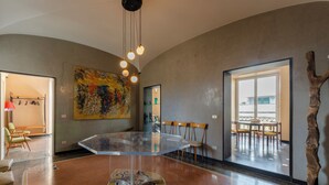 A spacious room with a glass-top table, chairs, a large abstract painting, and a view of the outdoors. - JOIVY Exclusive 3-bedroom flat near Cathedral of Genoa (Genoa)