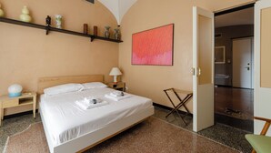 A hotel room with a bed, bedside table, lamp, and a shelf with decorative items. - JOIVY Exclusive 3-bedroom flat near Cathedral of Genoa (Genoa)