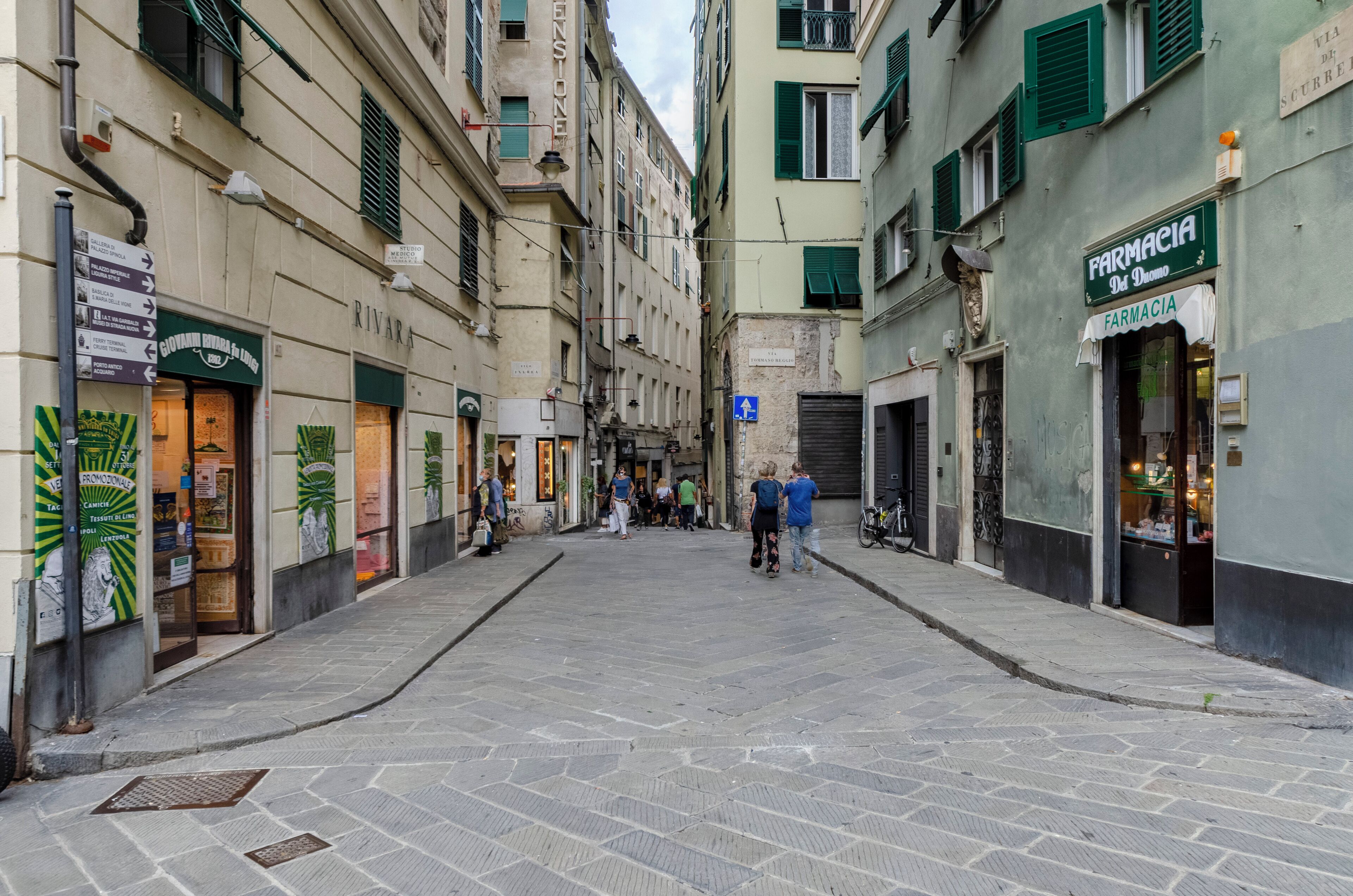 Une rue étroite bordée de boutiques des deux côtés, notamment une pharmacie et un restaurant.