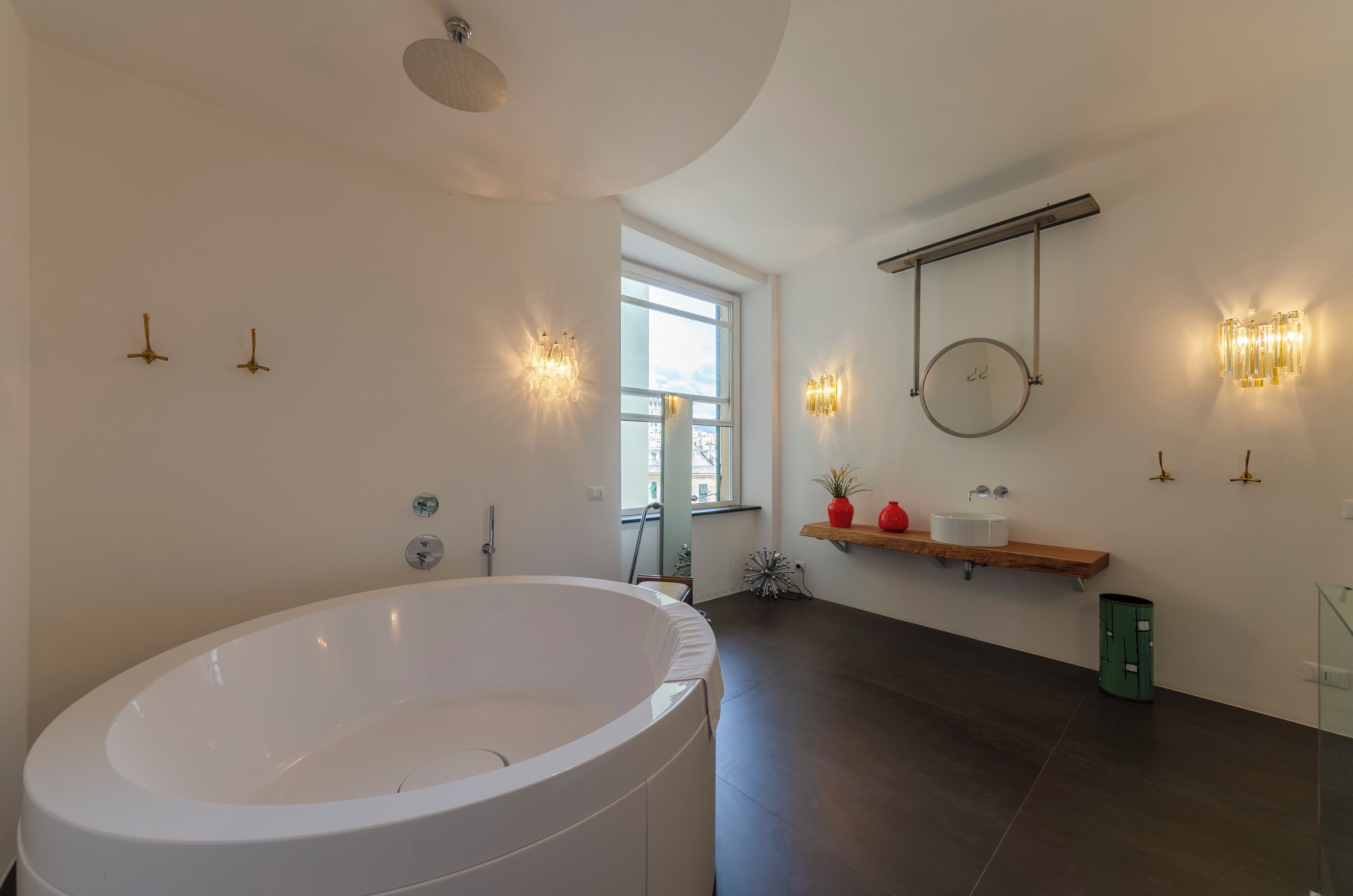 Une salle de bain moderne avec une grande baignoire, un miroir rond et des appliques murales.