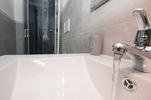 A modern bathroom with a white sink, chrome faucet, and a glass shower enclosure.
