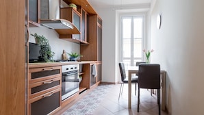 A modern kitchen with wooden cabinets, a stove, and a dining area with a table and chairs. - JOIVY Elegant 1 Br Flat Next To Milano Centrale (Milan)