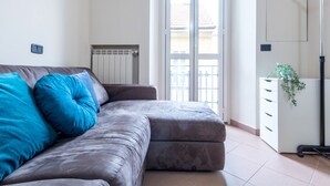 A modern living room with a grey sofa, blue cushions, a white cabinet, and a plant. - JOIVY Elegant 1 Br Flat Next To Milano Centrale (Milan)