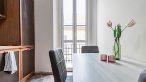 A dining area with a table, chairs, a vase with flowers, and a view of the outside through a window. - JOIVY Elegant 1 Br Flat Next To Milano Centrale (Milan)