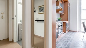 A modern kitchen with wooden cabinets, a stove, and a dining area with a chair. - JOIVY Elegant 1 Br Flat Next To Milano Centrale (Milan)
