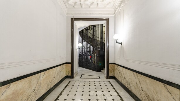 A hallway with a marble floor and white walls, leading to a staircase with a black railing. - JOIVY Elegant flat near Spianata Castelletto (Genoa)