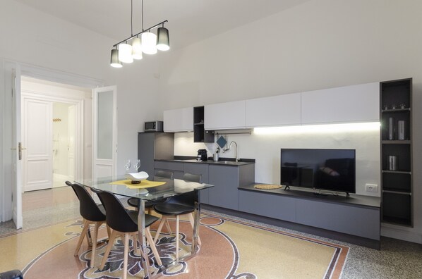 Una cucina moderna con zona pranzo, che include un tavolo in vetro, sedie nere e una TV a schermo piatto.