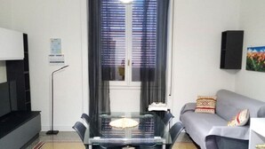 A compact living space with a dining table, two chairs, a sofa, and a TV. - JOIVY Elegant flat near Spianata Castelletto (Genoa)