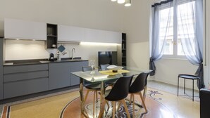 A modern kitchen with a glass dining table, black chairs, and a built-in oven. - JOIVY Elegant flat near Spianata Castelletto (Genoa)