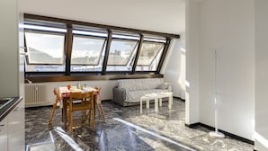 A modern living room with a dining area, large windows with a view, a sofa, and a floor lamp.