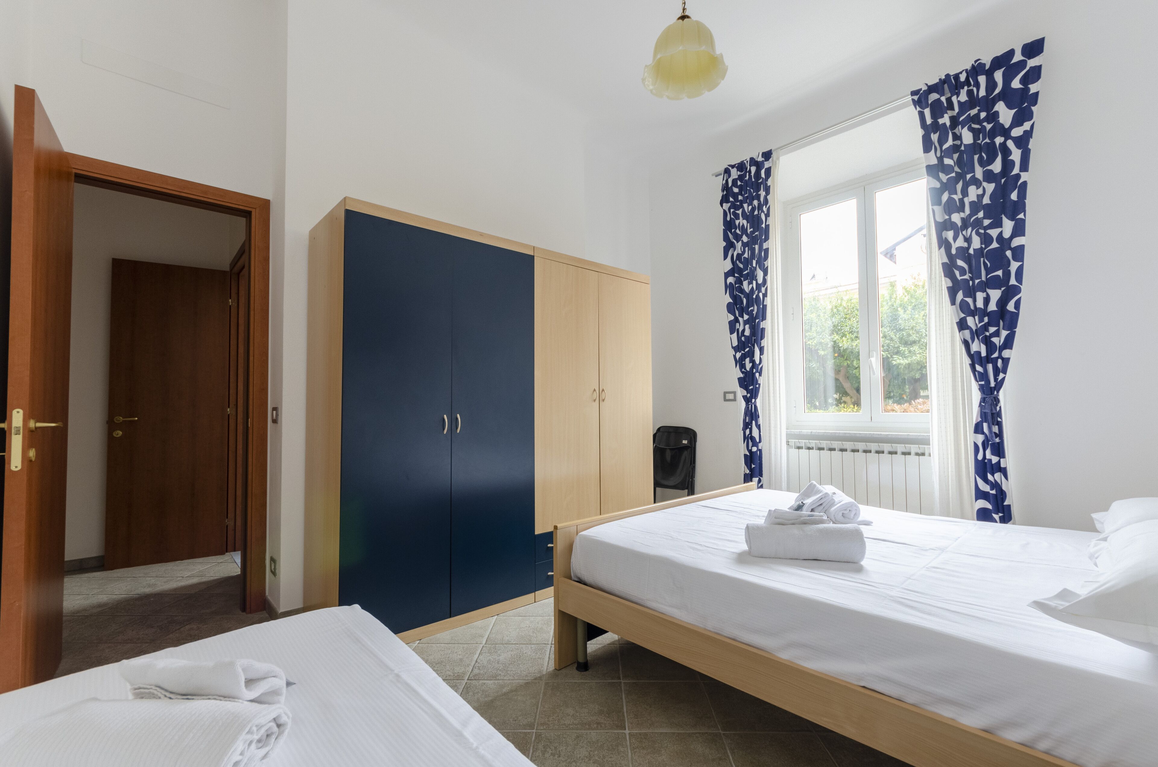 A hotel room with a bed, a wardrobe, a radiator, and a window with curtains.
