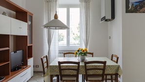A dining area with a table set for four, a television on a cabinet, and a radiator under the window. - JOIVY Family Apt For 6, Right Next To The Beach (Finale Ligure)