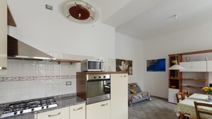 A kitchen with a gas stove, oven, microwave, and a dining area with a table and chairs. - JOIVY Family Apt For 6, Right Next To The Beach (Finale Ligure)
