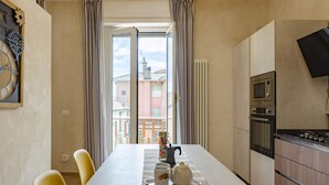 A modern kitchen with a dining area, a large window with curtains, and a view of buildings outside. - JOIVY Chic Chiavari Apt With 2 Spacious Terraces (Chiavari)