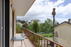 Un balcón con mesa y sillas, barandilla y vistas a edificios y árboles.