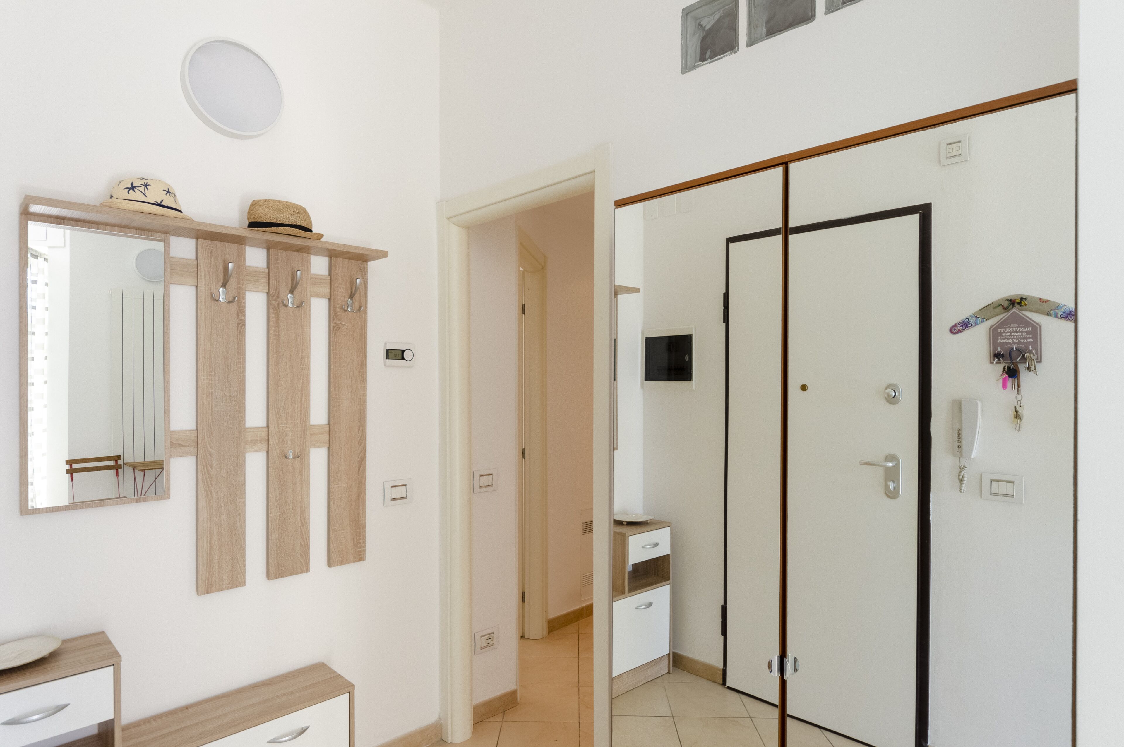 A hotel room with a wooden coat rack, a mirror, a wardrobe, and a small desk with drawers.
