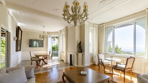 A spacious living room with a chandelier, a dining area, and large windows offering a view. - JOIVY Splendid Villa With Orange Trees And Stunning View (Santa Margherita Ligure)