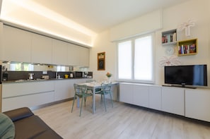Une cuisine moderne avec des meubles blancs, une table à manger avec des chaises, un téléviseur et une fenêtre donnant sur un beau paysage.