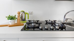 Une cuisine moderne équipée d’une cuisinière à gaz, d’un évier, d’une plante en pot, d’une planche à découper en bois et d’une bouilloire.