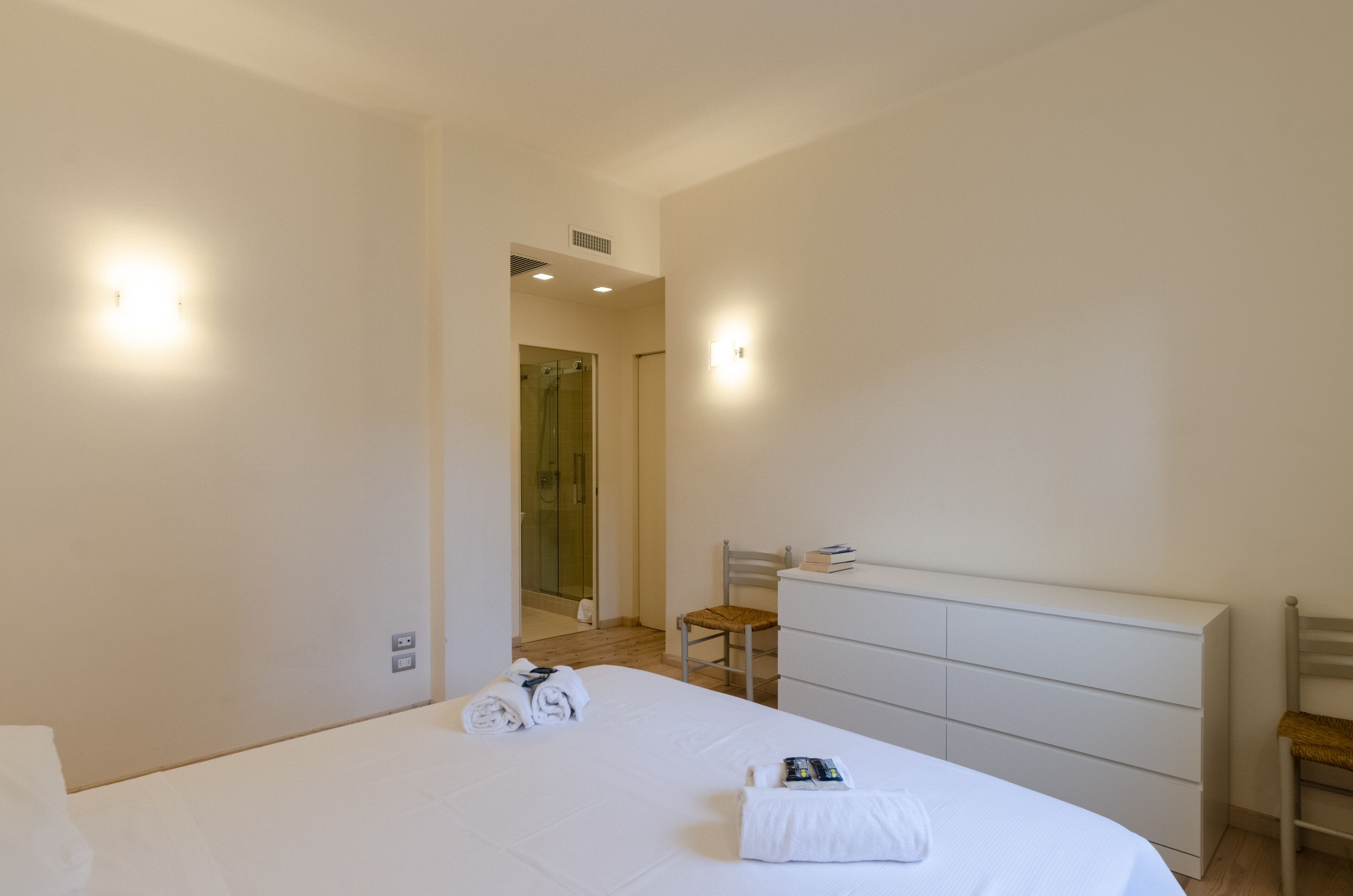 A hotel room with a large bed, a white dresser, a chair, and a shower area.