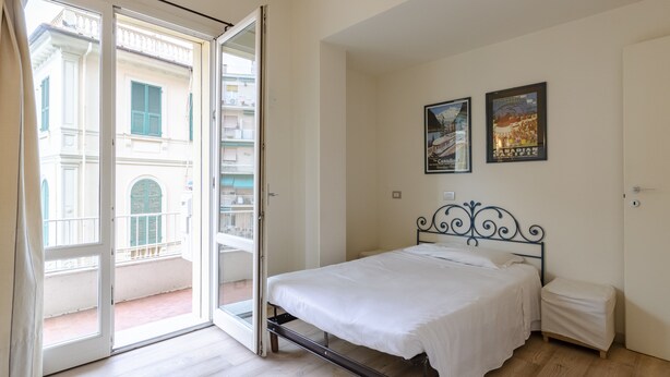 A bedroom with a bed, a small bedside table, a door, and a balcony with a view of buildings. - JOIVY Bright 3-bedroom apartment in Santa Margherita (Santa Margherita Ligure)