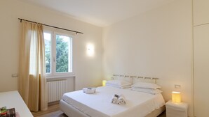 A clean, minimalist bedroom with a large bed, bedside lamps, and a view of greenery outside. - JOIVY Bright 3-bedroom apartment in Santa Margherita (Santa Margherita Ligure)