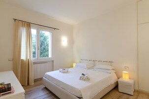 Camera da letto pulita e dal design minimalista, con un letto grande, lampade ai comodini e vista sul verde.