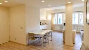 A modern, well-lit room with a wooden floor, a dining table with chairs, a small kitchenette, and a window with curtains. - JOIVY Bright 3-bedroom apartment in Santa Margherita (Santa Margherita Ligure)