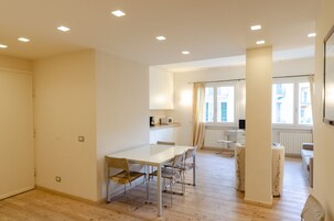 Una stanza moderna e luminosa, con pavimento in legno, un tavolo da pranzo con sedie, un angolo cottura e una finestra con tende.